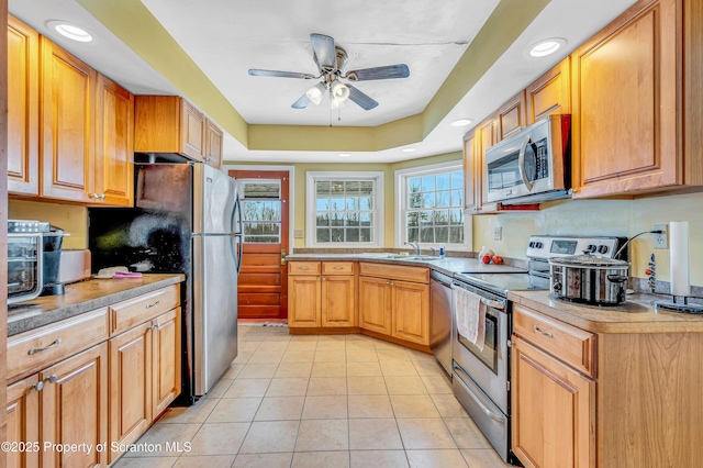 kitchen featuring light tile patterned floors, sink, ceiling fan, appliances with stainless steel finishes, and a tray ceiling