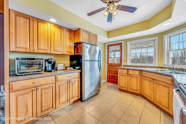 kitchen with sink, range, light tile patterned floors, stainless steel refrigerator, and a raised ceiling