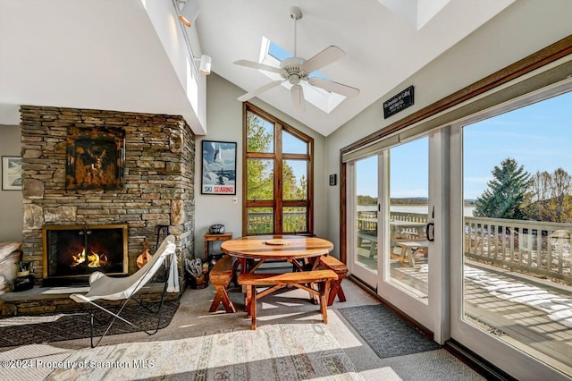 sunroom with ceiling fan, a stone fireplace, and lofted ceiling with skylight