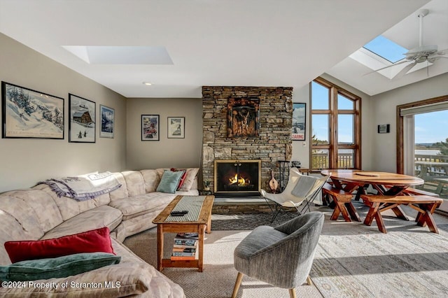 carpeted living room featuring vaulted ceiling with skylight, ceiling fan, and a fireplace