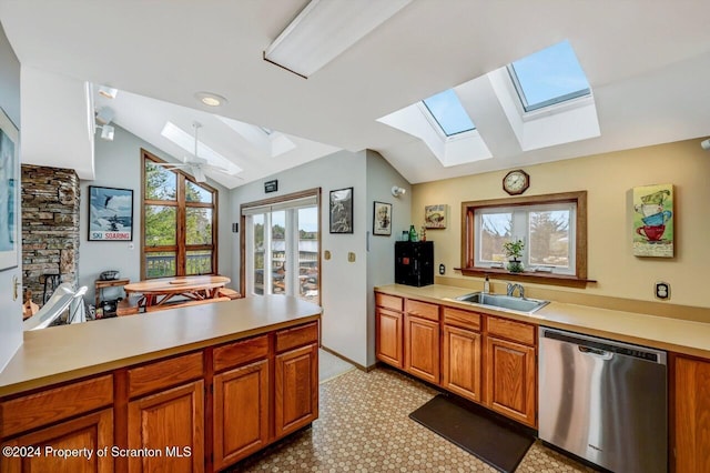 kitchen featuring dishwasher, lofted ceiling with skylight, sink, ceiling fan, and a fireplace