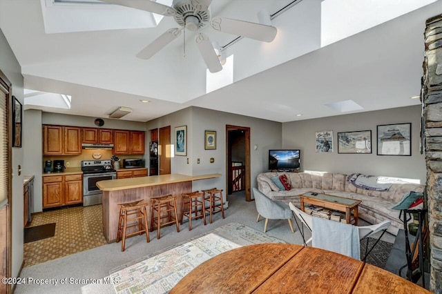 kitchen with a skylight, ceiling fan, a breakfast bar area, light colored carpet, and stainless steel electric stove