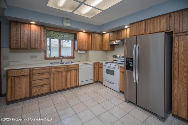 kitchen with light countertops, a sink, brown cabinets, under cabinet range hood, and white appliances