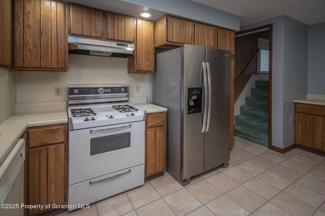 kitchen with stainless steel fridge, white gas stove, under cabinet range hood, dishwasher, and brown cabinets