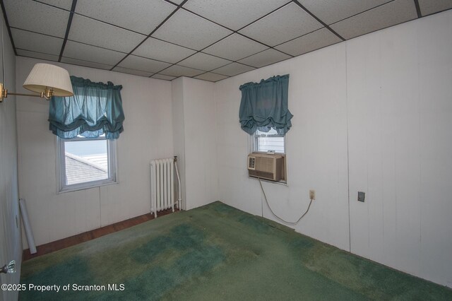 unfurnished bedroom featuring carpet flooring, cooling unit, a paneled ceiling, and radiator