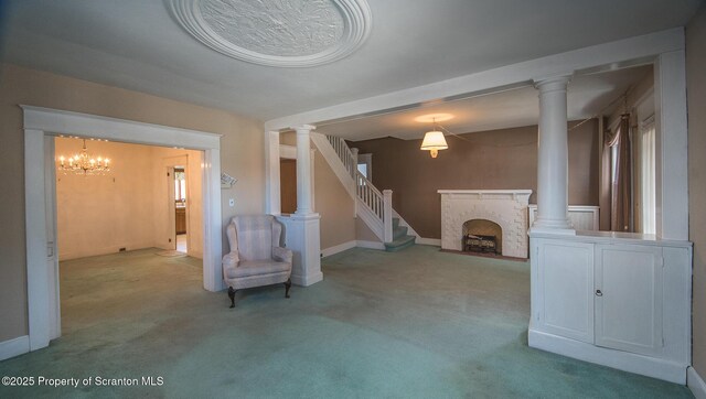 unfurnished living room with carpet, ornate columns, stairs, a fireplace, and a notable chandelier
