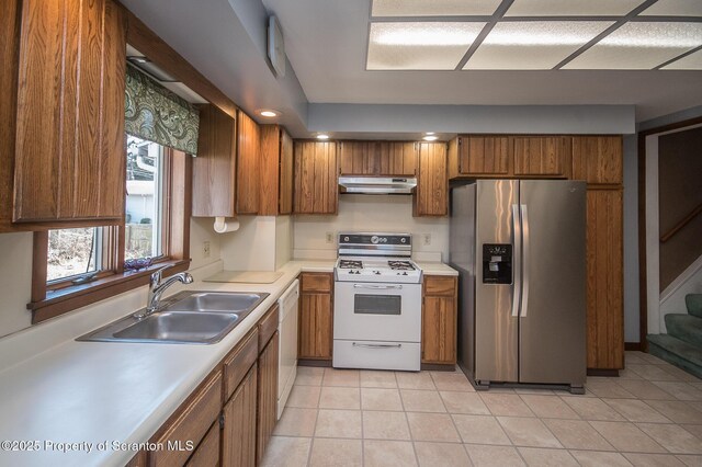 kitchen with white appliances, brown cabinetry, under cabinet range hood, and a sink