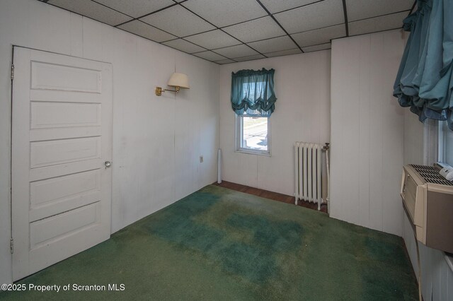 carpeted spare room featuring radiator and a drop ceiling