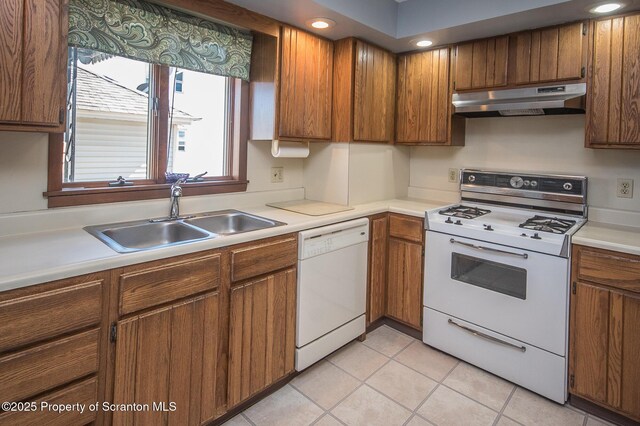 kitchen featuring light countertops, white appliances, under cabinet range hood, a sink, and brown cabinetry