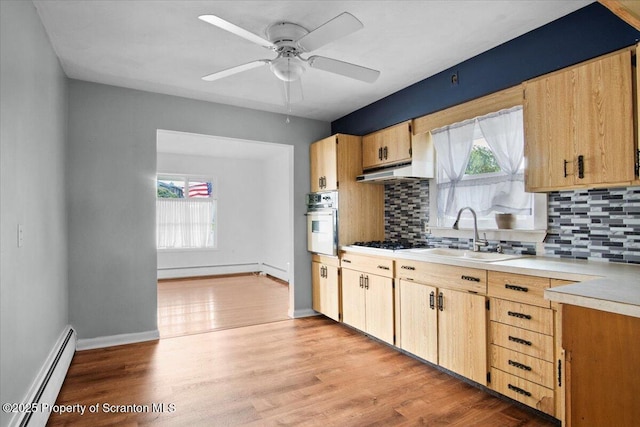 kitchen featuring baseboard heating, oven, tasteful backsplash, light countertops, and a sink