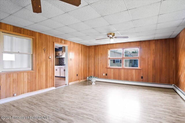spare room with a ceiling fan, wood finished floors, wood walls, a baseboard heating unit, and baseboards