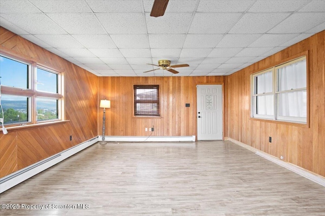 unfurnished living room featuring a ceiling fan, wood finished floors, baseboards, wood walls, and a drop ceiling