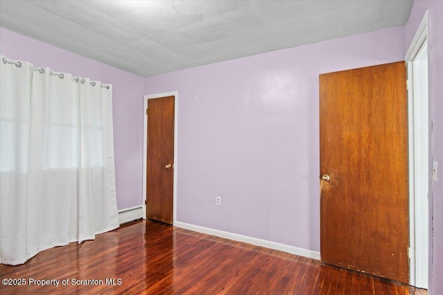 unfurnished bedroom featuring baseboard heating, wood finished floors, and baseboards