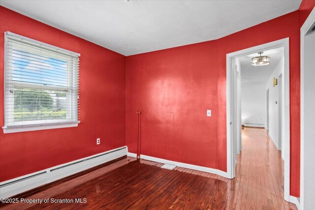 empty room with a baseboard radiator, wood finished floors, and baseboards