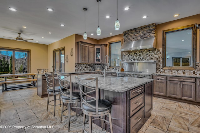 815 Oak St, Archbald, PA 18403 - kitchen featuring light stone countertops, a breakfast bar, ceiling fan, wall chimney exhaust hood, and backsplash