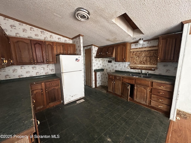 kitchen with lofted ceiling, dark countertops, freestanding refrigerator, a sink, and wallpapered walls