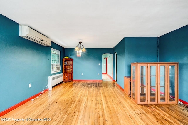 unfurnished room featuring radiator, a notable chandelier, a wall mounted AC, and light wood-type flooring