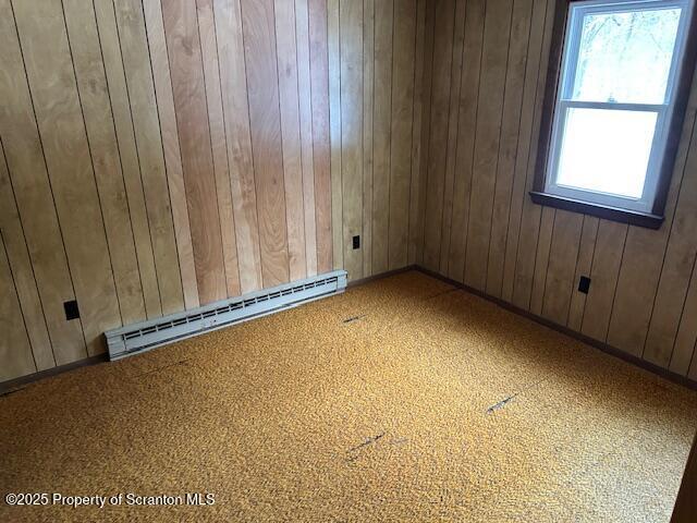 empty room with wood walls, a baseboard radiator, and baseboards