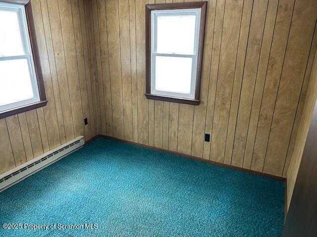 unfurnished room featuring a healthy amount of sunlight, wood walls, carpet, and a baseboard heating unit