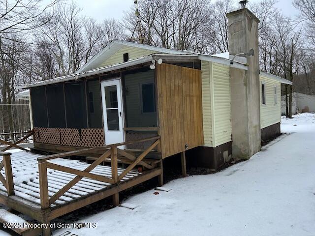 view of snowy exterior with a chimney and a sunroom