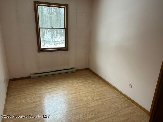 empty room with a baseboard heating unit, light wood-type flooring, and baseboards