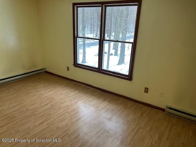 empty room featuring baseboards, baseboard heating, and light wood-style floors