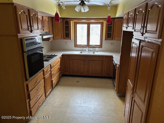 kitchen with cooktop, glass insert cabinets, oven, light countertops, and a sink