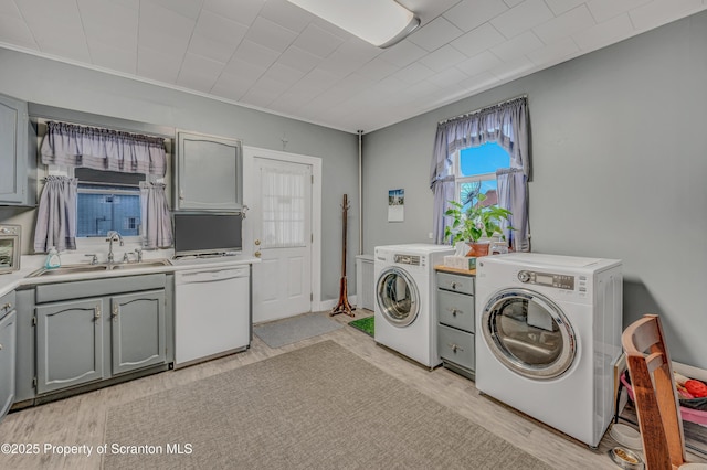 clothes washing area with laundry area, washing machine and dryer, light wood-type flooring, and a sink