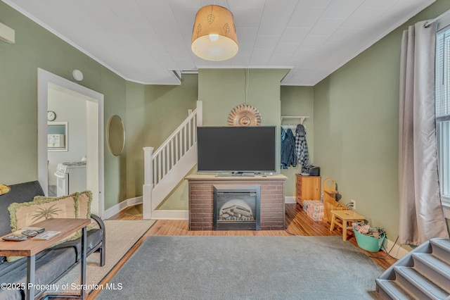 living area featuring a brick fireplace, crown molding, baseboards, stairs, and wood finished floors