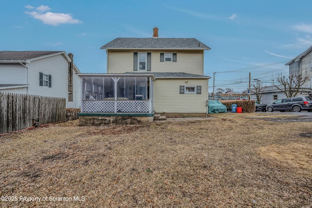 rear view of house featuring a chimney, fence, and a sunroom