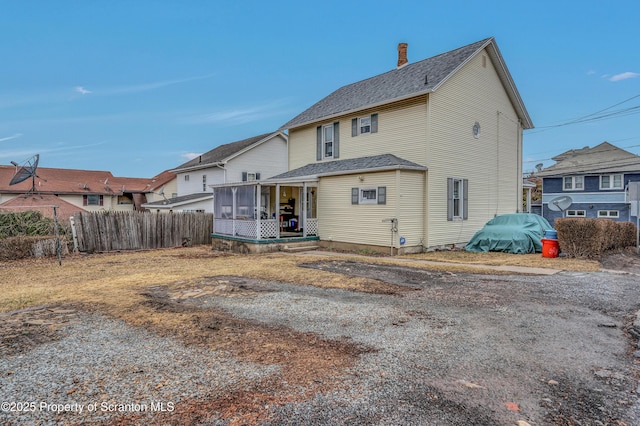 view of front of home featuring a shingled roof, fence, a sunroom, and a chimney