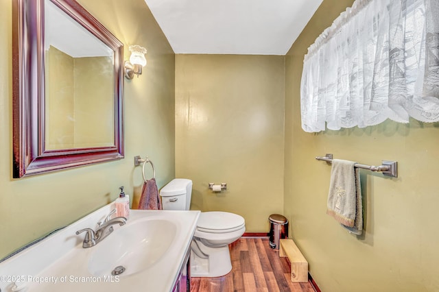 half bathroom with baseboards, toilet, wood finished floors, and vanity