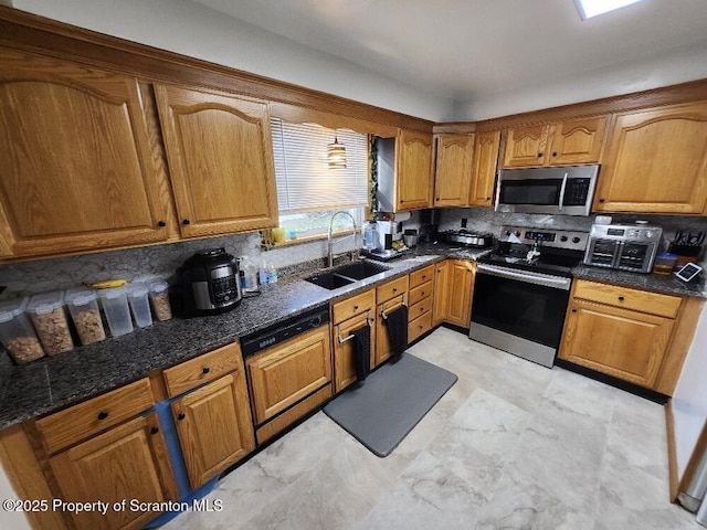 kitchen with stainless steel appliances, tasteful backsplash, brown cabinetry, a sink, and dark stone countertops