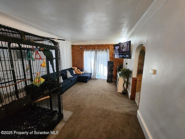 carpeted living area with arched walkways, wood walls, and baseboards