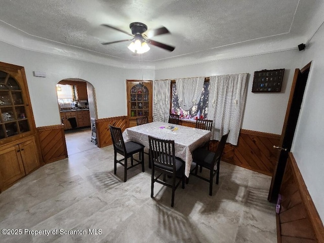 dining room featuring a wainscoted wall, wooden walls, and arched walkways