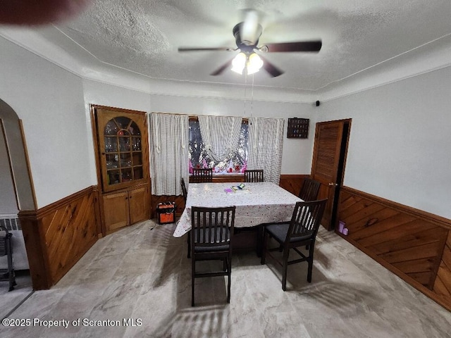 dining room with a wainscoted wall, a ceiling fan, a textured ceiling, and wood walls