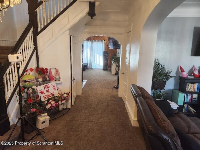 hallway with carpet floors, stairs, and arched walkways