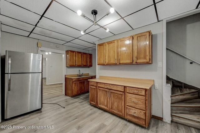 kitchen with a paneled ceiling, a sink, light wood-style floors, light countertops, and freestanding refrigerator