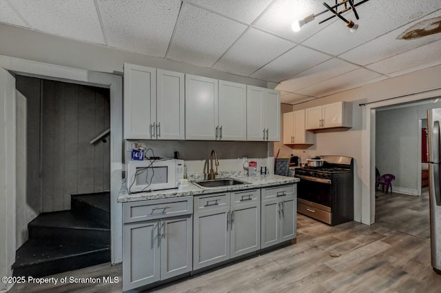 kitchen featuring a drop ceiling, stainless steel appliances, a sink, light wood-type flooring, and gray cabinets