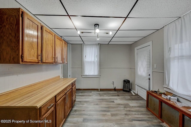 interior space with light wood-style flooring, brown cabinetry, and a drop ceiling