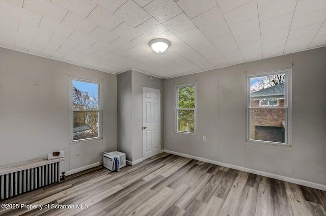 spare room featuring baseboards, radiator heating unit, and wood finished floors