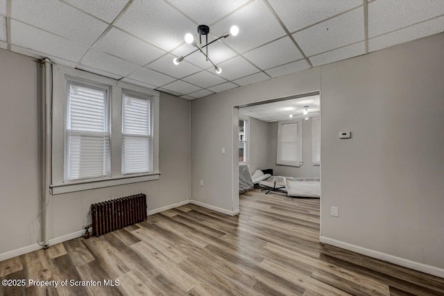 empty room with radiator, baseboards, a paneled ceiling, and wood finished floors