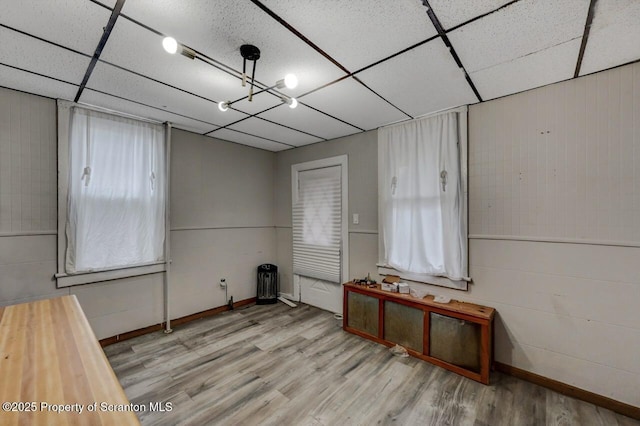 interior space with baseboards, a drop ceiling, and wood finished floors