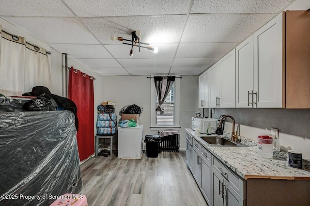 kitchen featuring light wood finished floors, light countertops, a paneled ceiling, white cabinetry, and a sink