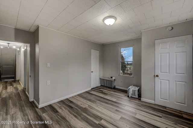 unfurnished bedroom featuring radiator heating unit, wood finished floors, and baseboards