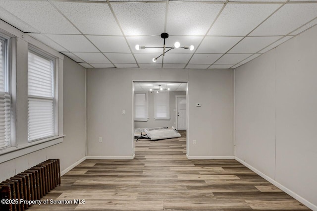 spare room featuring a chandelier, a drop ceiling, wood finished floors, and radiator