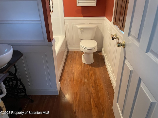 bathroom featuring wood-type flooring, a tub to relax in, and toilet