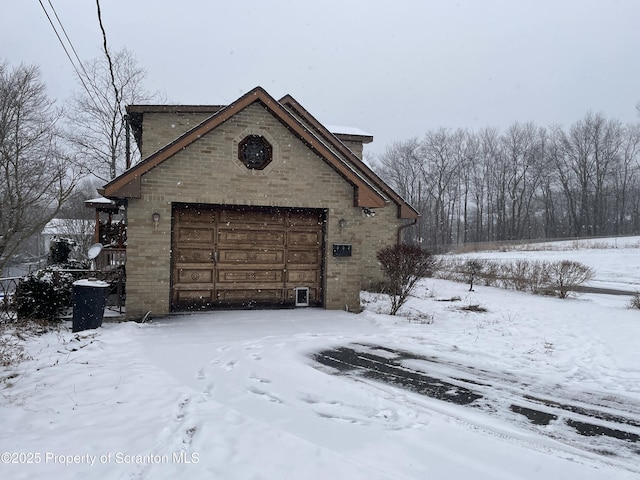 snow covered property with a garage and brick siding