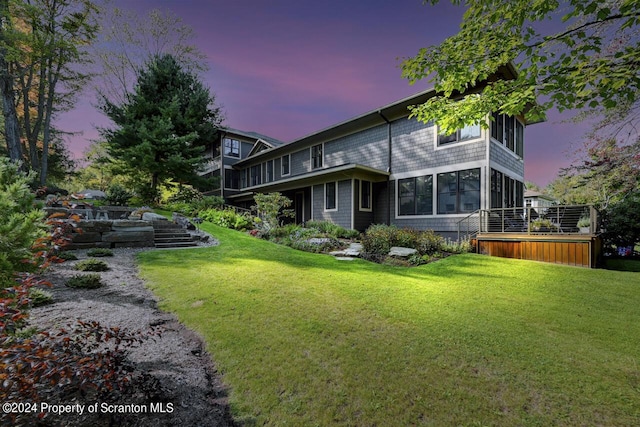 back house at dusk with a yard and a sunroom