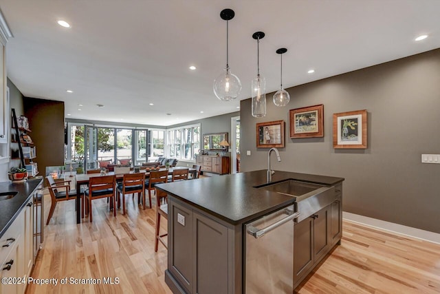 kitchen featuring sink, stainless steel dishwasher, an island with sink, pendant lighting, and light wood-type flooring